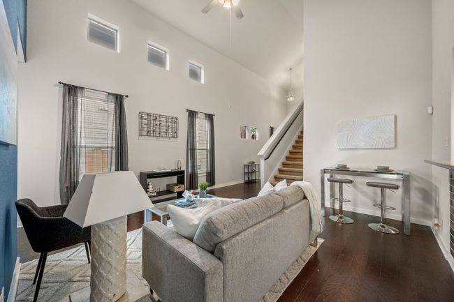 Living room featuring baseboards, a ceiling fan, wood finished floors, stairway, and a towering ceiling | Image 8