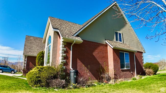 View of side of home featuring roof with shingles, a lawn, stucco siding, and brick siding | Image 16