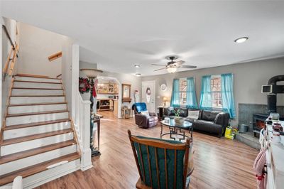 Living room featuring ceiling fan, light laminate floors, and a wood burning stove | Image 3