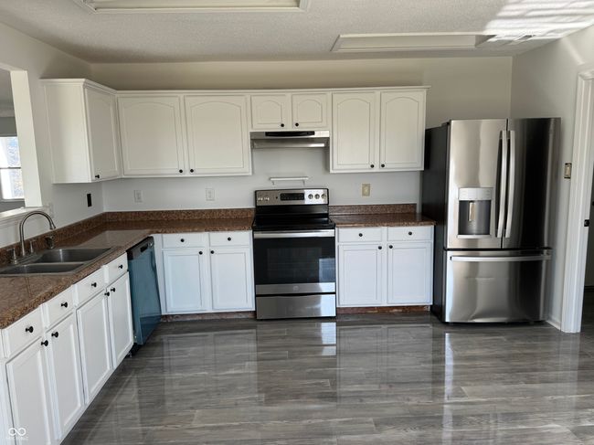 kitchen with under cabinet range hood, a textured ceiling, a sink, white cabinets, and appliances with stainless steel finishes | Image 6