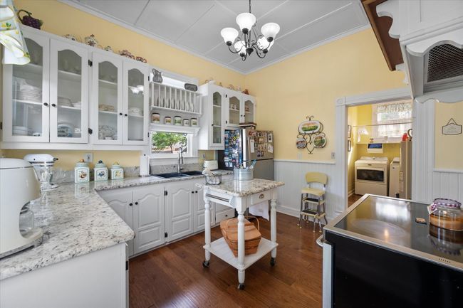 Kitchen with washer and dryer, a sink, a chandelier, a wainscoted wall, and white cabinetry | Image 13