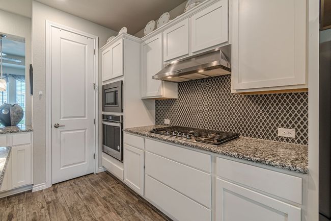 Kitchen with stainless steel appliances, extractor fan, white cabinets, decorative backsplash, and dark wood-style flooring | Image 12