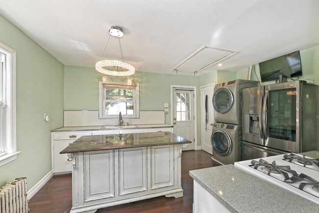 Kitchen with a sink, radiator heating unit, stainless steel fridge, stovetop, and stacked washer / dryer | Image 10