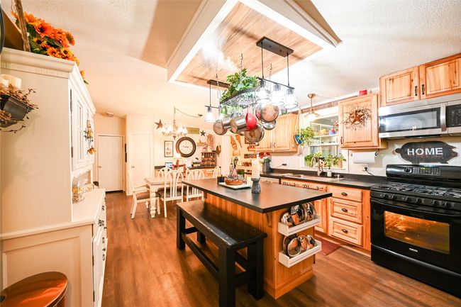 Kitchen with black gas stove, stainless steel microwave, dark countertops, a sink, and dark wood finished floors | Image 21