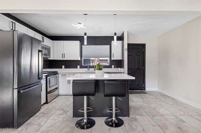 Kitchen featuring a kitchen island, stainless steel appliances, light countertops, white cabinets, and a kitchen bar | Image 11