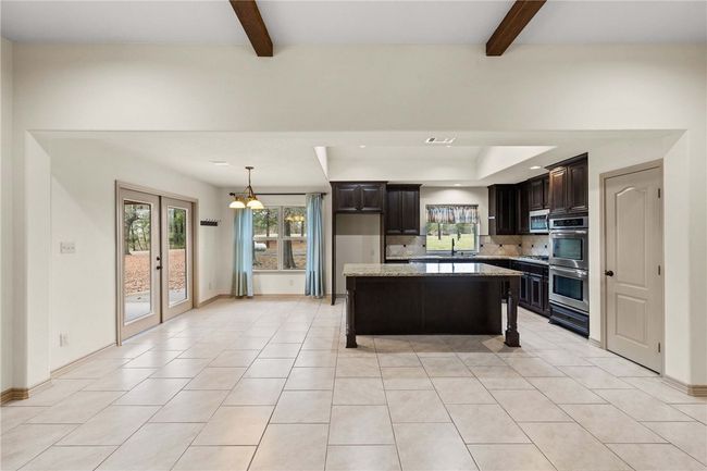 Kitchen featuring a center island, backsplash, light tile patterned flooring, dark brown cabinetry, and light stone countertops | Image 7