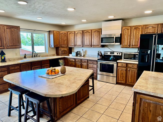 Kitchen with a breakfast bar area, brown cabinetry, appliances with stainless steel finishes, light countertops, and a sink | Image 4
