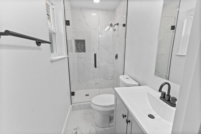 Bathroom with marble look tile flooring, toilet, a marble finish shower, baseboards, and vanity | Image 14