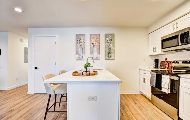 Kitchen with a breakfast bar, an island with sink, light wood-style flooring, stainless steel appliances, and a sink | Image 9