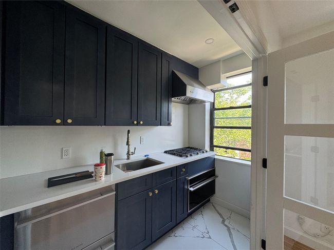 Kitchen featuring exhaust hood, stainless steel gas stovetop, light marble finish flooring, light countertops, and dark cabinets | Image 6