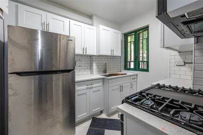 Kitchen featuring white cabinetry, island exhaust hood, stainless steel fridge, backsplash, and sink | Image 1