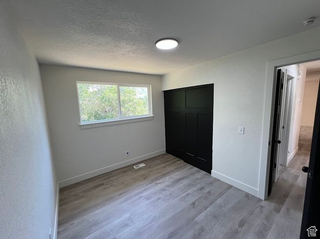 Unfurnished bedroom with light wood-type flooring, a textured wall, a textured ceiling, and a closet | Image 21