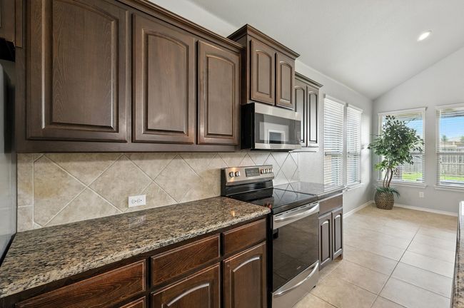 Kitchen with stainless steel appliances, dark stone countertops, dark brown cabinets, backsplash, and lofted ceiling | Image 7