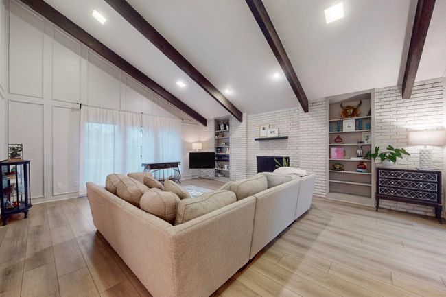 Living room featuring a fireplace, brick wall, vaulted ceiling with beams, and light wood-style floors | Image 7