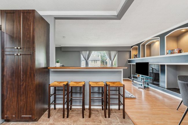 Kitchen with a kitchen breakfast bar, a textured ceiling, dark brown cabinets, ornamental molding, and wood finished floors | Image 13