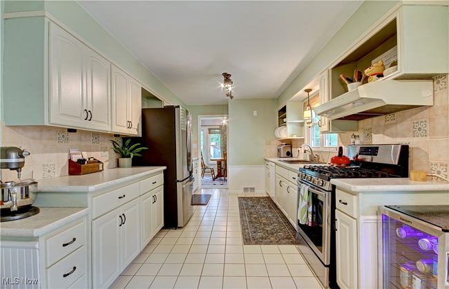 Kitchen featuring stainless steel appliances, open shelves, under cabinet range hood, light tile patterned floors, and wine cooler | Image 17