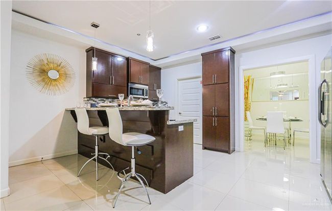 Kitchen with kitchen peninsula, decorative backsplash, light stone countertops, a breakfast bar, and decorative light fixtures | Image 9