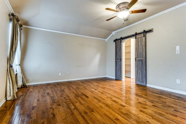 Unfurnished bedroom with vaulted ceiling, crown molding, a barn door, and hardwood / wood-style flooring | Image 9