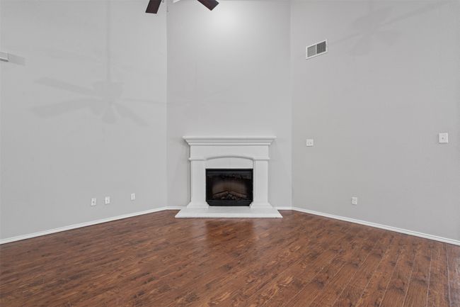 Unfurnished living room with ceiling fan, wood finished floors, a fireplace with raised hearth, and a high ceiling | Image 20