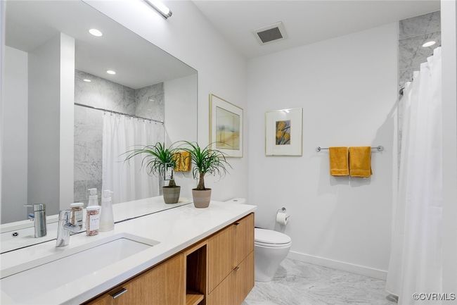 Bright third en suite bathroom with wood grain vanity, tiled floor and tiled shower. | Image 38