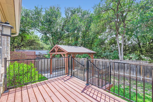 Wooden deck featuring a fenced backyard with gate opening up to green space behind | Image 33