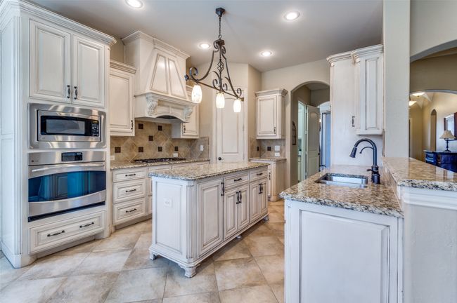 Kitchen with premium range hood, decorative backsplash, arched walkways, stainless steel appliances, and a sink | Image 14