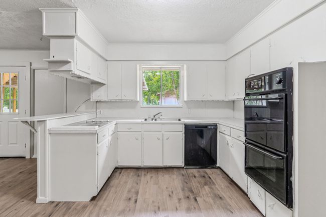 Kitchen with black appliances, a textured ceiling, ornamental molding, light wood-style flooring, and light countertops | Image 15
