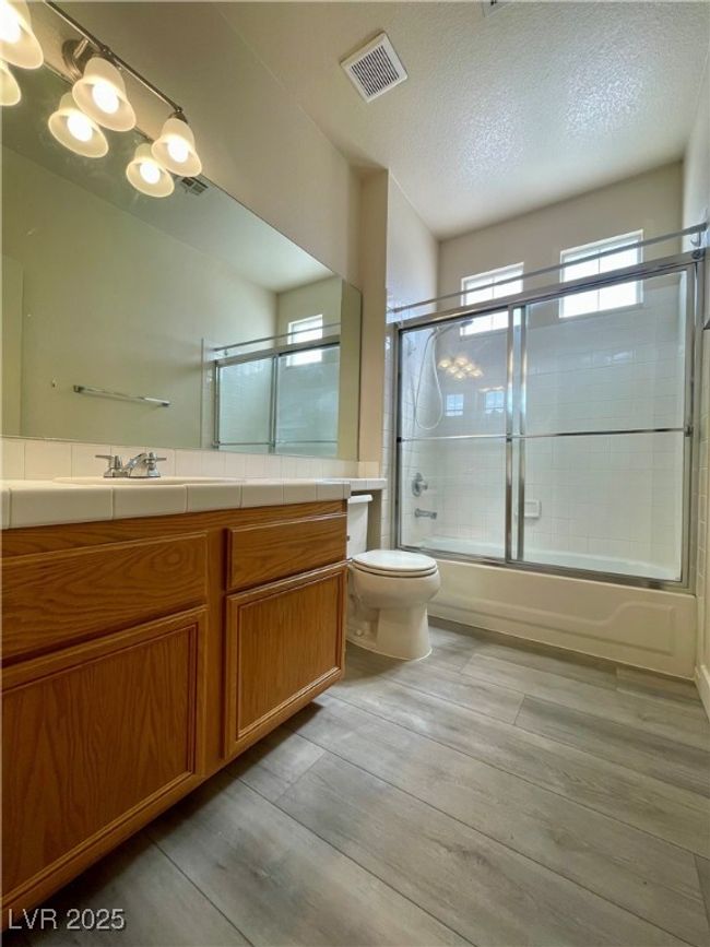 Full bath featuring vanity, toilet, visible vents, enclosed tub / shower combo, and wood finished floors | Image 5