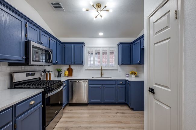 Kitchen with tasteful backsplash, a sink, stainless steel appliances, light wood finished floors, and blue cabinets | Image 13