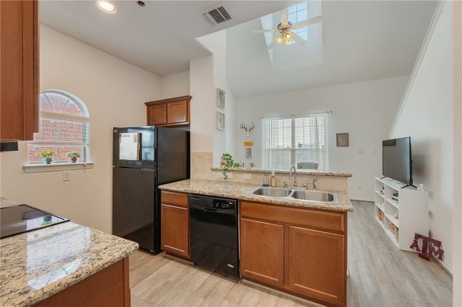 Kitchen featuring black appliances, lofted ceiling, a peninsula, light wood-type flooring, and brown cabinets | Image 10