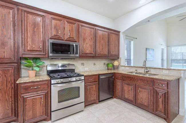 Kitchen featuring a sink, light stone countertops, appliances with stainless steel finishes, and a wealth of natural light | Image 14