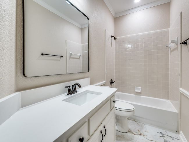 Bathroom featuring crown molding, vanity with new marble counter and undermount sink, new mirror, tub / shower combo, and marble finish tile flooring | Image 21