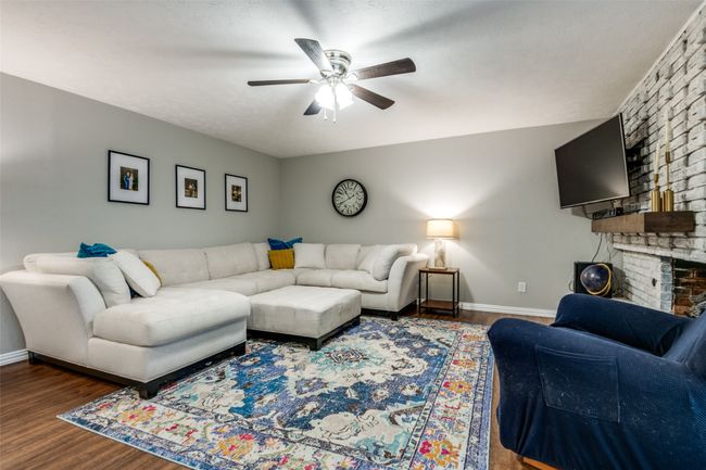 Living area with a fireplace, ceiling fan, and wood finished floors. | Image 4