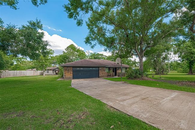 Charming single-story brick home with a spacious front yard and mature trees. Features a wide driveway leading to a two-car garage, offering plenty of parking and outdoor space. | Image 34