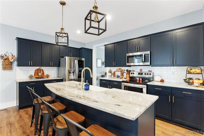 Kitchen with backsplash, a kitchen bar, appliances with stainless steel finishes, light stone countertops, and light wood finished floors | Image 15