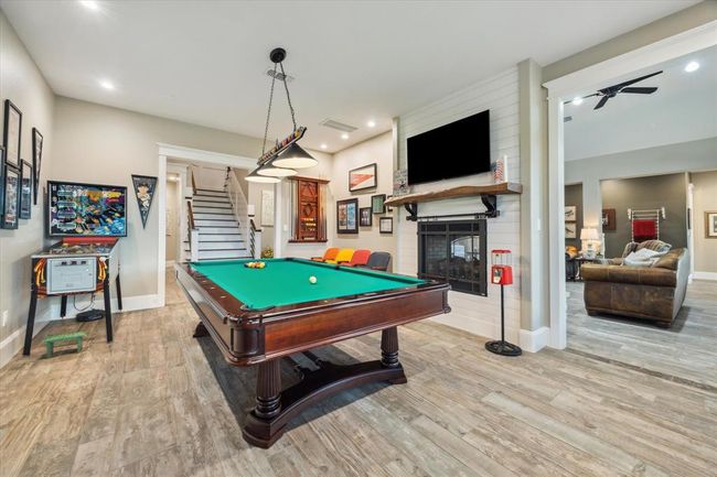 The game room is an ideal space for a pool table, featuring a double-sided gas fireplace that adds warmth and ambiance. Built-in cabinets provide ample storage, while recessed lighting, integrated into the home's custom lighting system, ensures the perfect setting for both play and relaxation. | Image 15