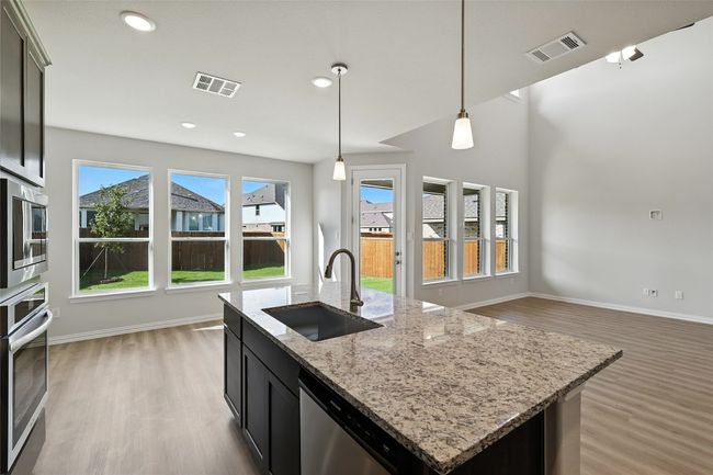 Kitchen featuring stainless steel appliances, light wood finished floors, decorative light fixtures, open floor plan, and an island with sink | Image 4
