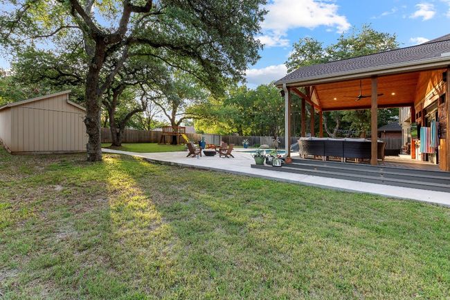 Fenced backyard with an outdoor living space, a playground, a deck, a ceiling fan, and an outbuilding | Image 38