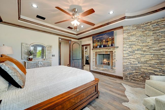 Bedroom featuring crown molding, a fireplace, a tray ceiling, recessed lighting, and wood finished floors | Image 22