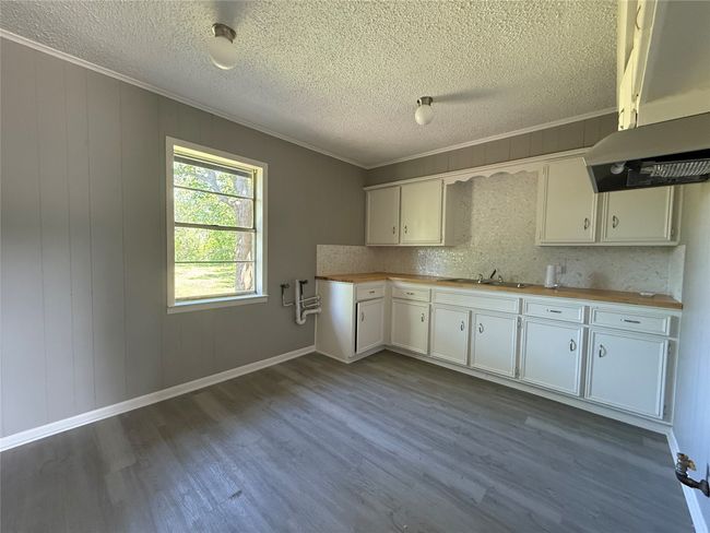 Kitchen with a textured ceiling, dark wood-style floors, white cabinetry, and wooden counters | Image 5