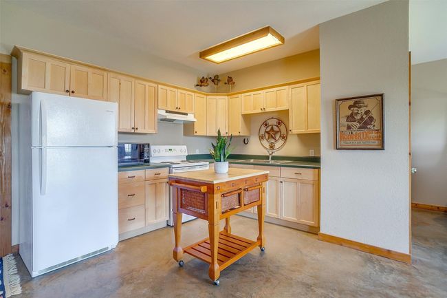 Kitchen featuring dark countertops, light brown cabinets, under cabinet range hood, and white appliances | Image 30