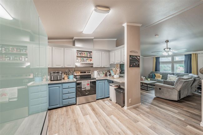 Kitchen with stainless steel electric stove, under cabinet range hood, crown molding, blue cabinets, and white cabinetry | Image 11