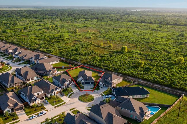 This photo shows a modern home in a quiet cul-de-sac, highlighted by a red outline. It is surrounded by similar homes and bordered by a large, scenic green space, offering privacy and a natural backdrop. | Image 45