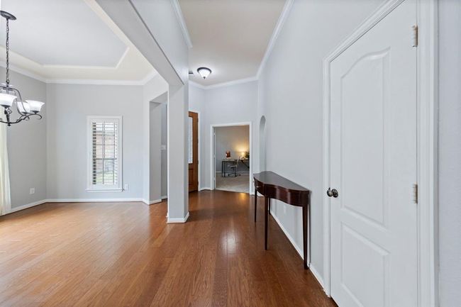 The entryway features warm wood floors, elegant crown molding, and a view into the formal dining area and home office—creating a bright, welcoming first impression. | Image 6