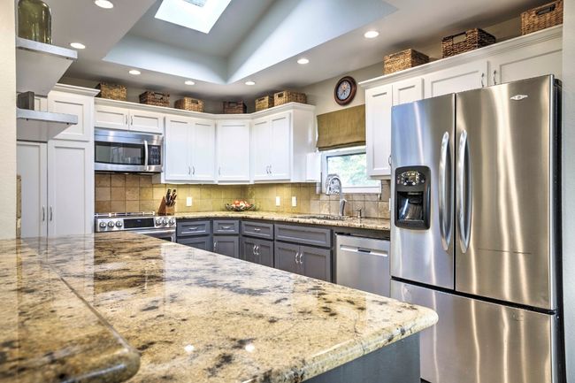 Kitchen from behind bar area featuring white cabinetry, stainless steel appliances, a raised ceiling, a sink, and a skylight | Image 19