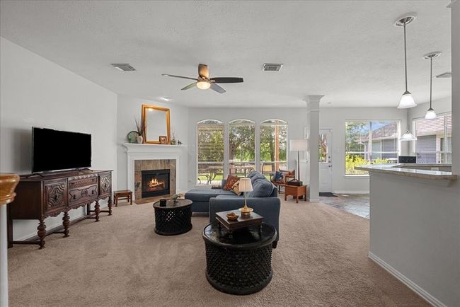 Bright, open-concept living area with a cozy fireplace and large windows while connecting seamlessly to the kitchen with a breakfast bar. | Image 5