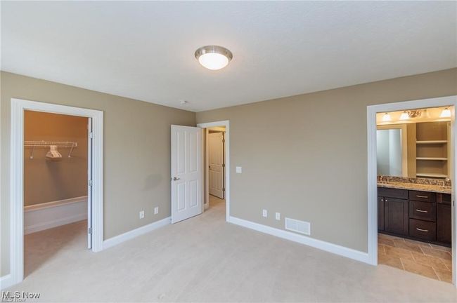 Unfurnished bedroom featuring a walk in closet, visible vents, light colored carpet, and baseboards | Image 4