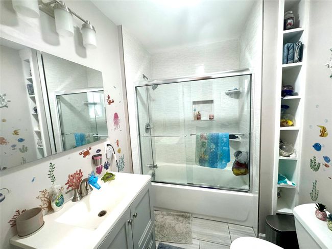 Full bathroom with vanity, bath / shower combo with glass door, and toilet | Image 5