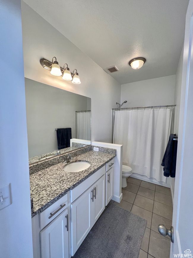 Full bathroom featuring toilet, a textured ceiling, tile patterned flooring, shower / bath combo with shower curtain, and vanity | Image 16