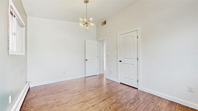 Empty room with visible vents, baseboards, baseboard heating, light wood-style floors, and an inviting chandelier | Image 17